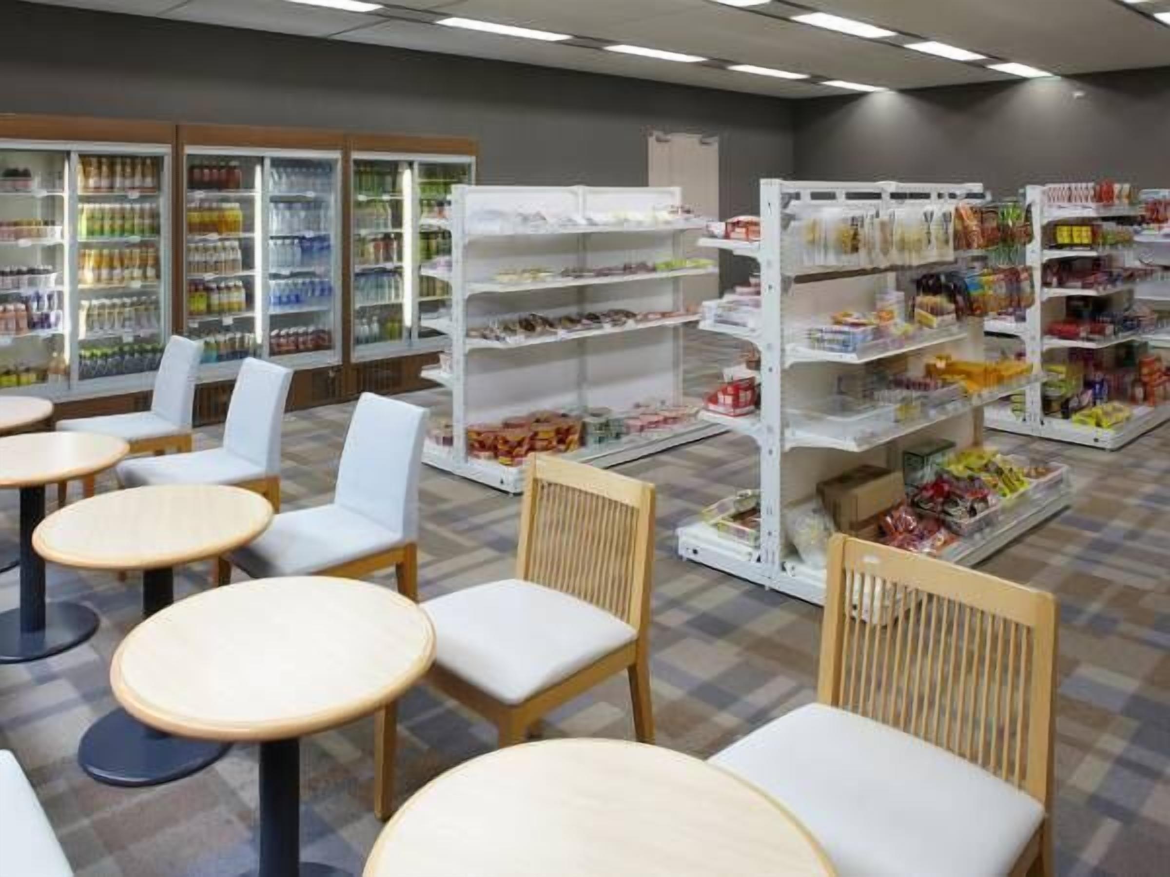 A clean, well-lit grocery store with white shelving, a few seating areas, and a variety of products on display.
