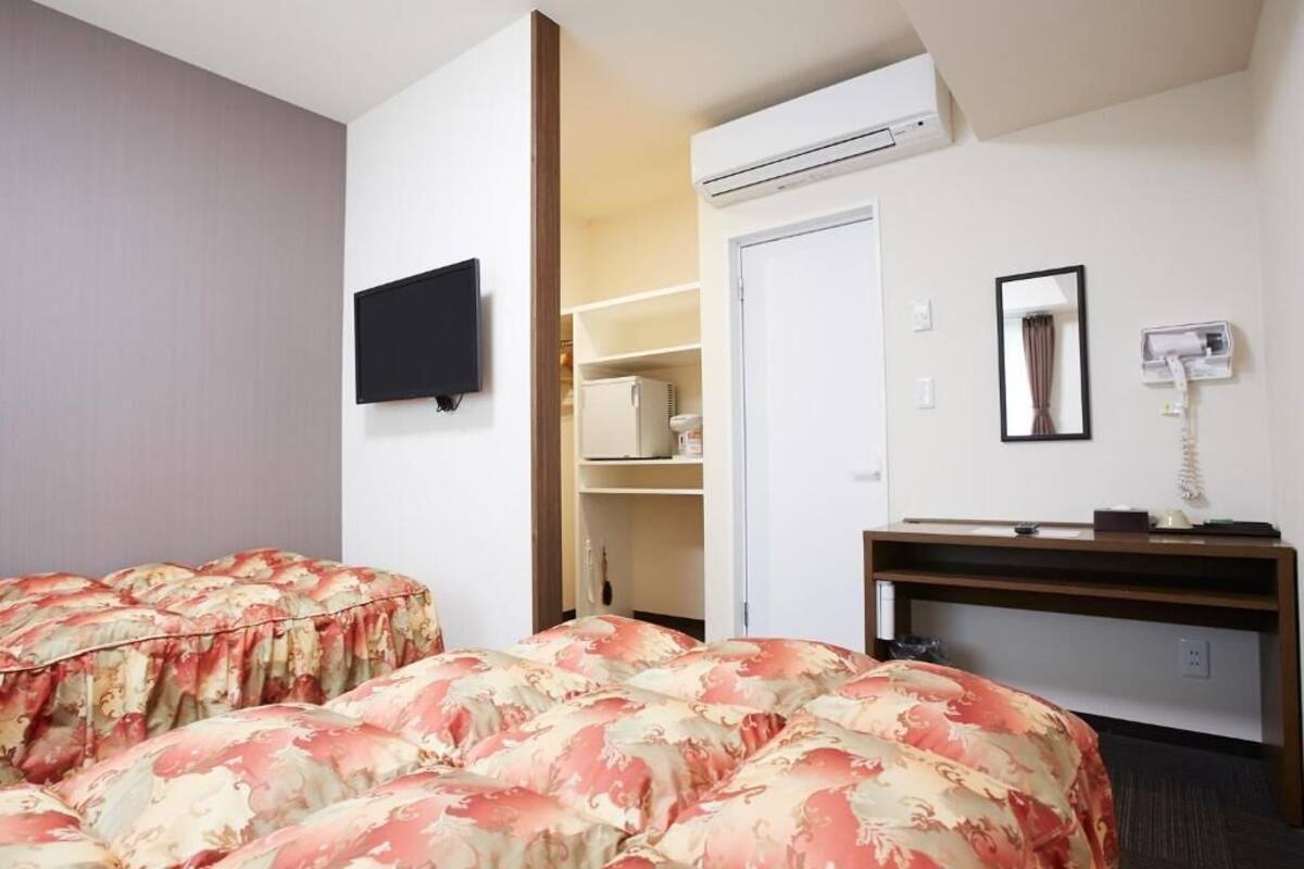 A hotel room with two beds, a TV, a desk with a telephone, and a wardrobe.