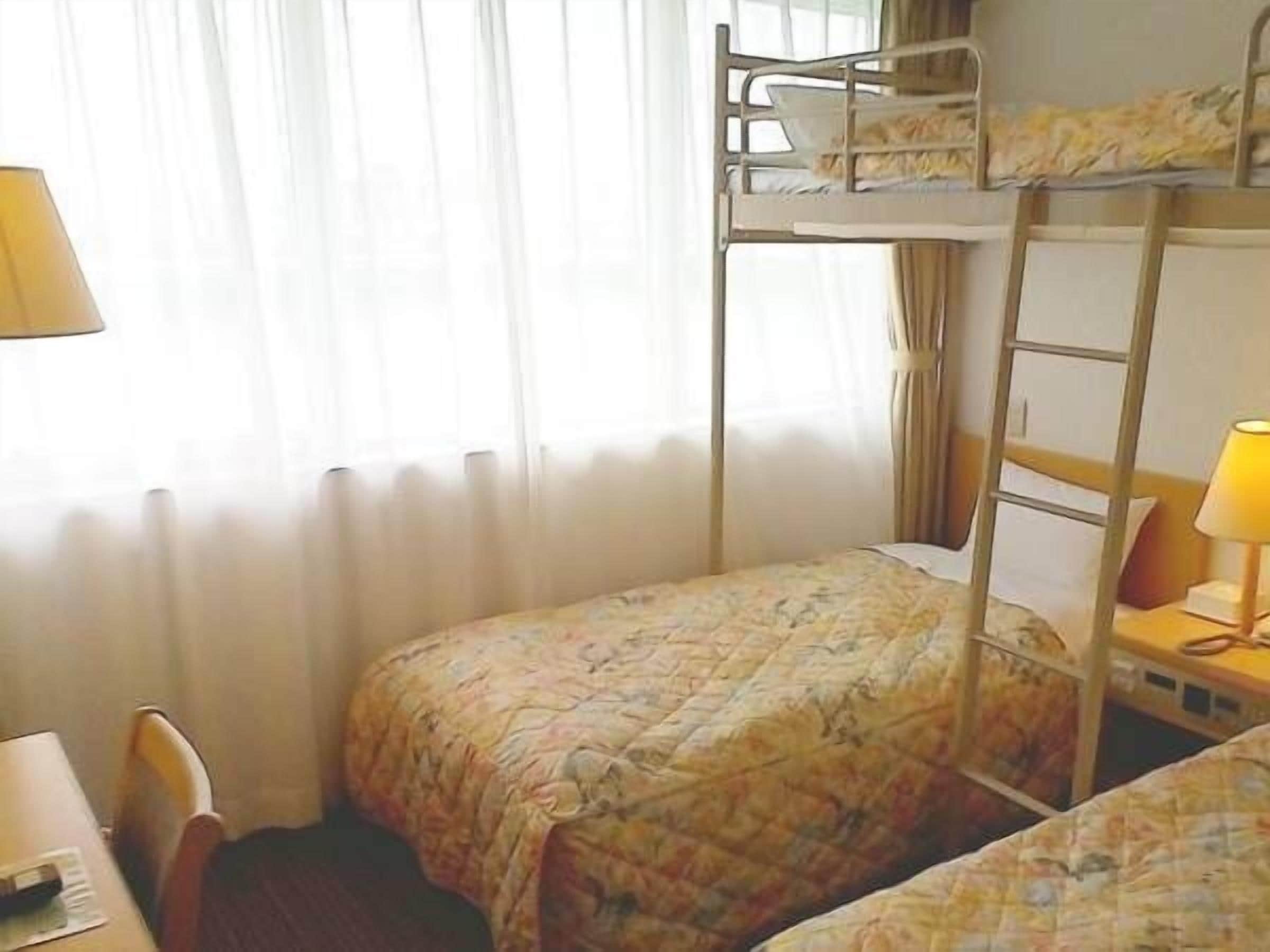 Habitación con literas, un escritorio, una silla, una lámpara y una ventana con cortinas.