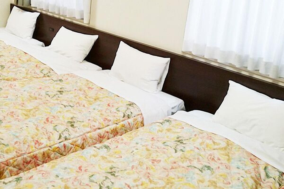 A hotel room with two beds, white bedding, floral-patterned bedspreads, and sheer curtains.