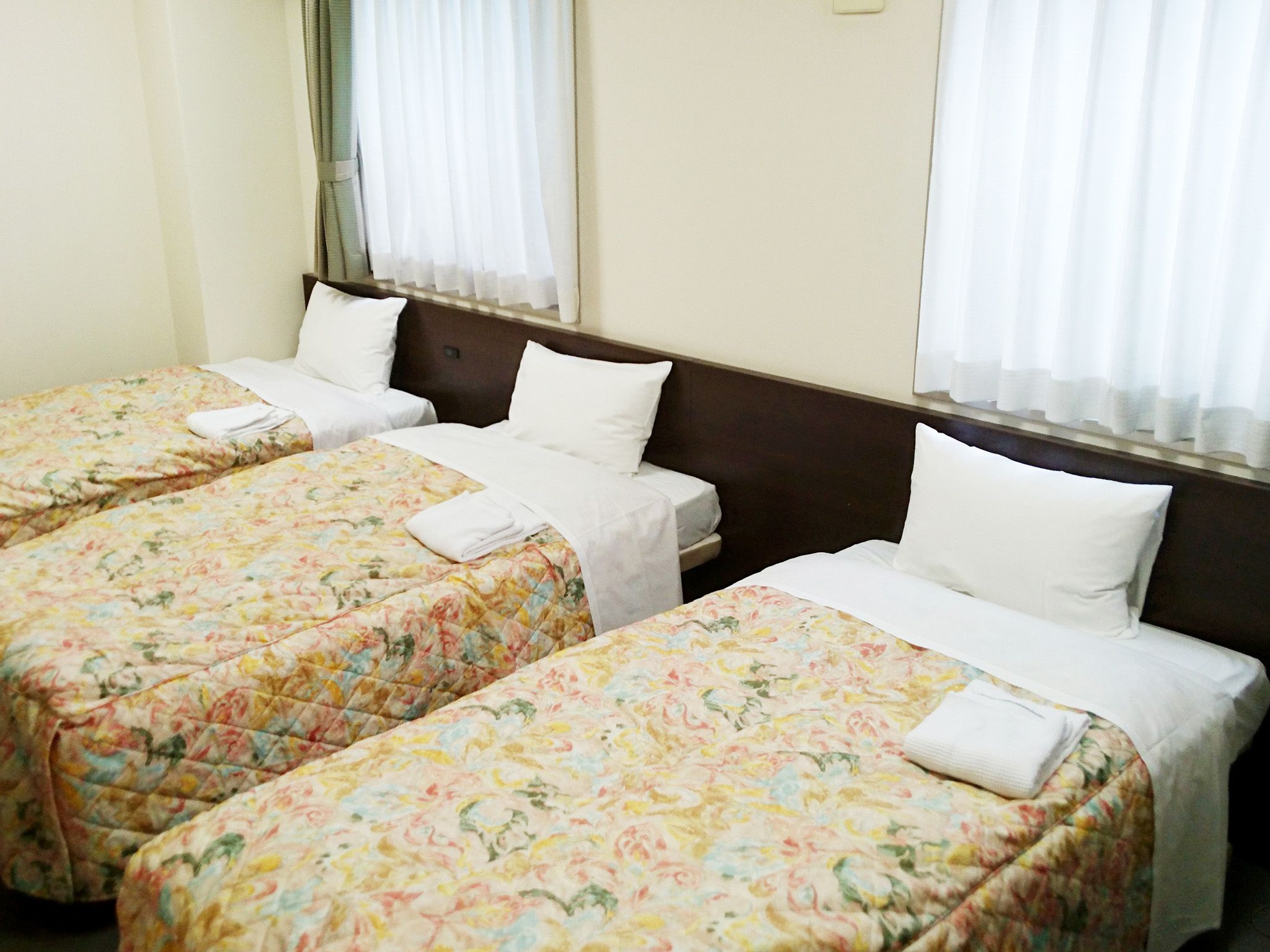 A hotel room with three single beds, each with a floral bedspread and white pillows.