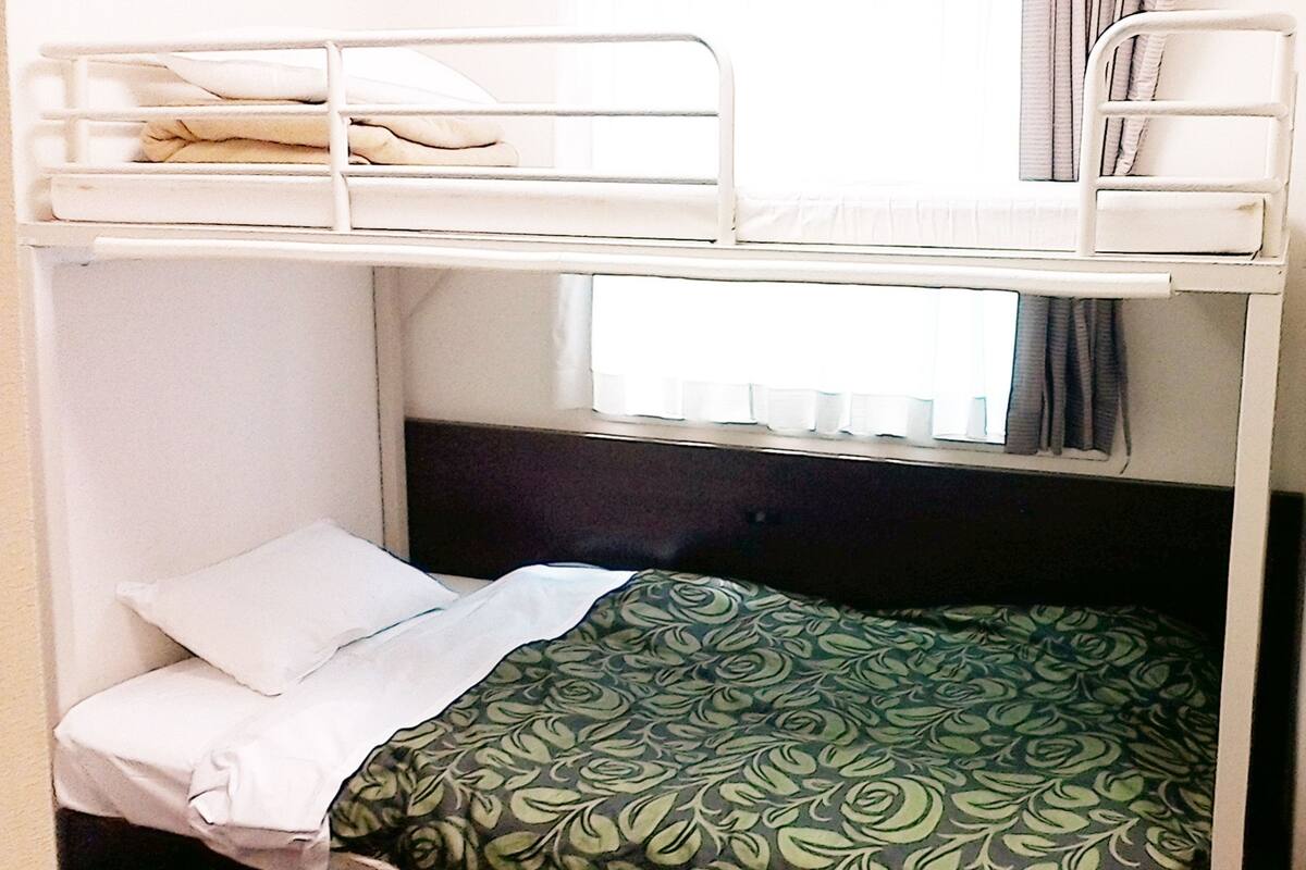 A bunk bed with a window above the lower bunk, a white pillow, and a patterned bedspread.