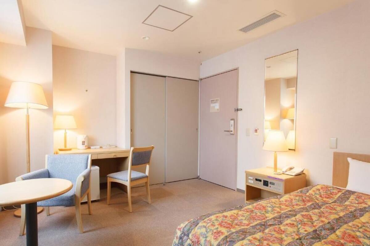 A hotel room with a bed, desk, chair, and bedside table.