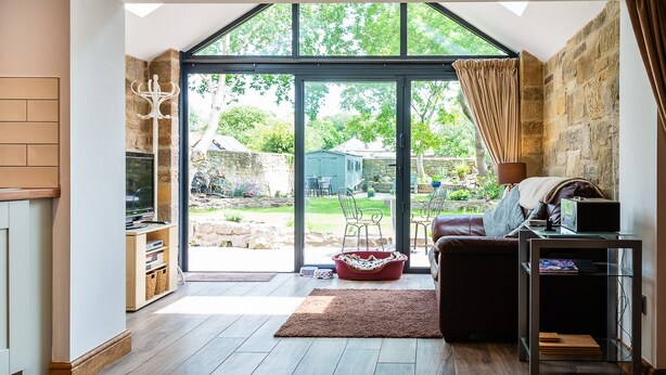 A cozy living room with a large sliding glass door leading to a garden, a fireplace, and a comfortable seating area. - CROSS HOUSE STUDIO Dog Friendly Stone Barn Conversion in the Heart of Warkworth (Warkworth)