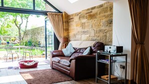 A cozy living room with a leather sofa, a glass coffee table, and a stone wall. - CROSS HOUSE STUDIO Dog Friendly Stone Barn Conversion in the Heart of Warkworth (Warkworth)