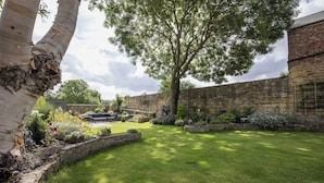 A well-maintained garden with a stone wall, a large tree, and a lawn. - CROSS HOUSE STUDIO Dog Friendly Stone Barn Conversion in the Heart of Warkworth (Warkworth)