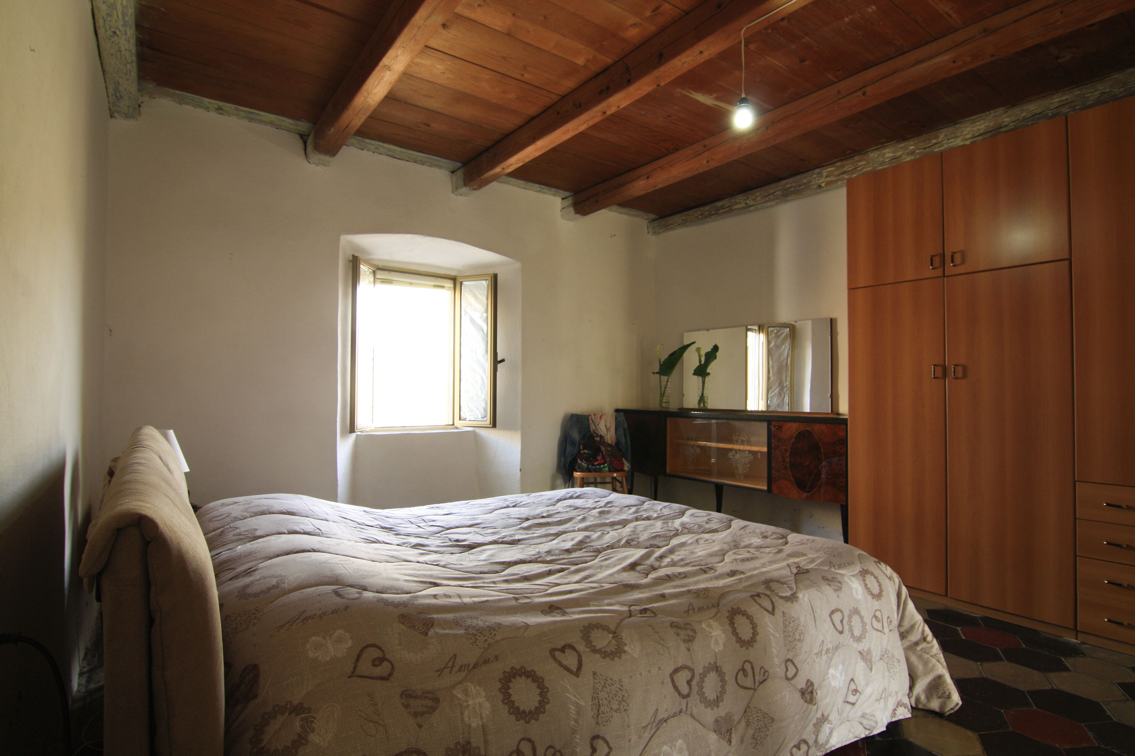 A bedroom with a bed, wooden wardrobe, a dresser, and a window.