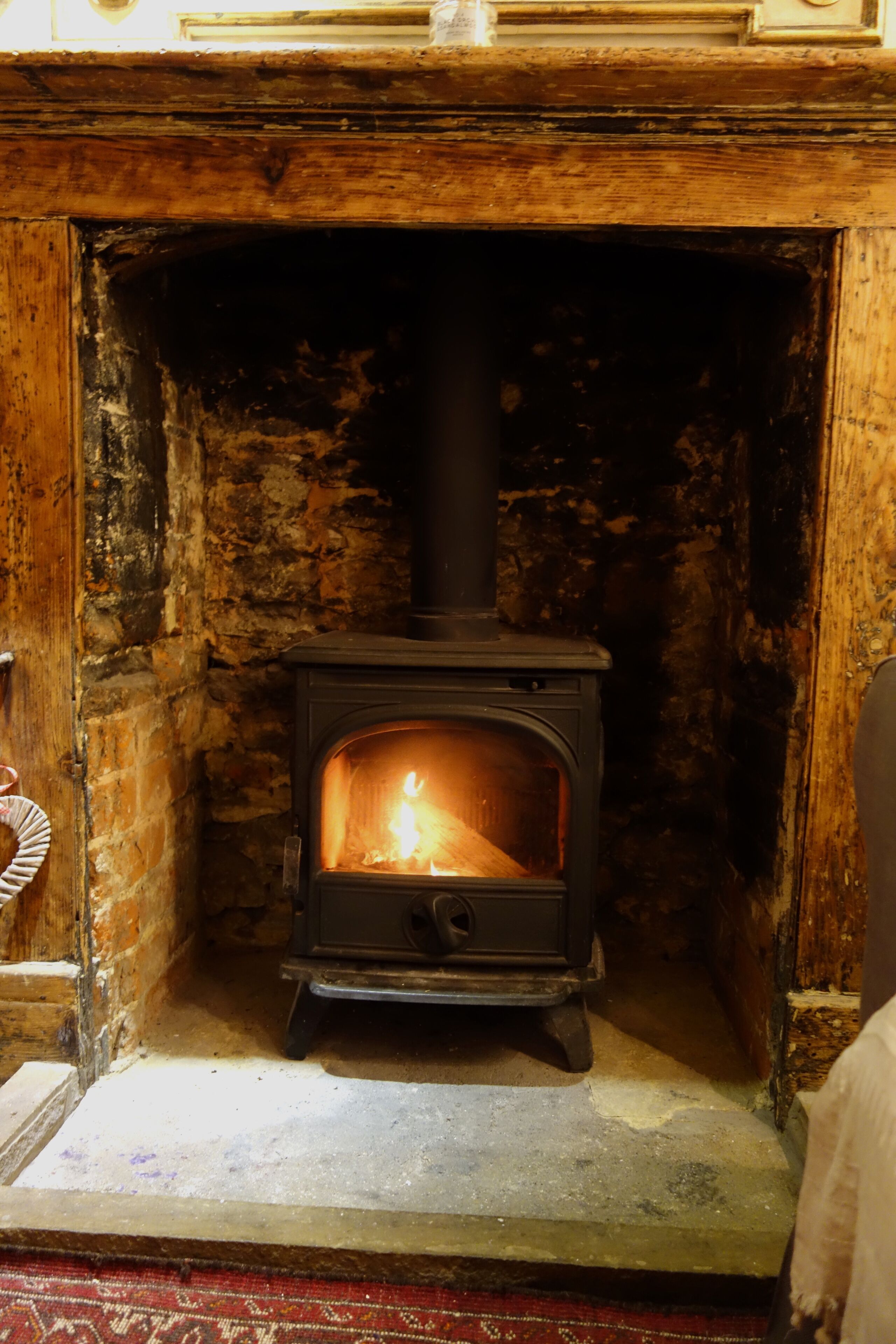 A wood-burning stove in a stone fireplace with a wooden frame and a red carpet.