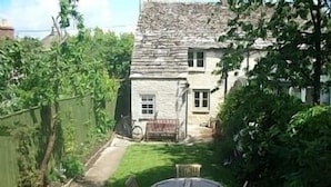 A stone house with a small garden, a wooden bench, and a table with chairs. - Charming, secluded, characterful cottage in the heart of Lechlade (Lechlade on Thames)