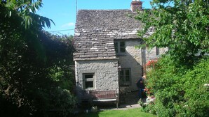 A stone house with a sloped roof, a chimney, and a small front porch with a bench. - Charming, secluded, characterful cottage in the heart of Lechlade (Lechlade on Thames)