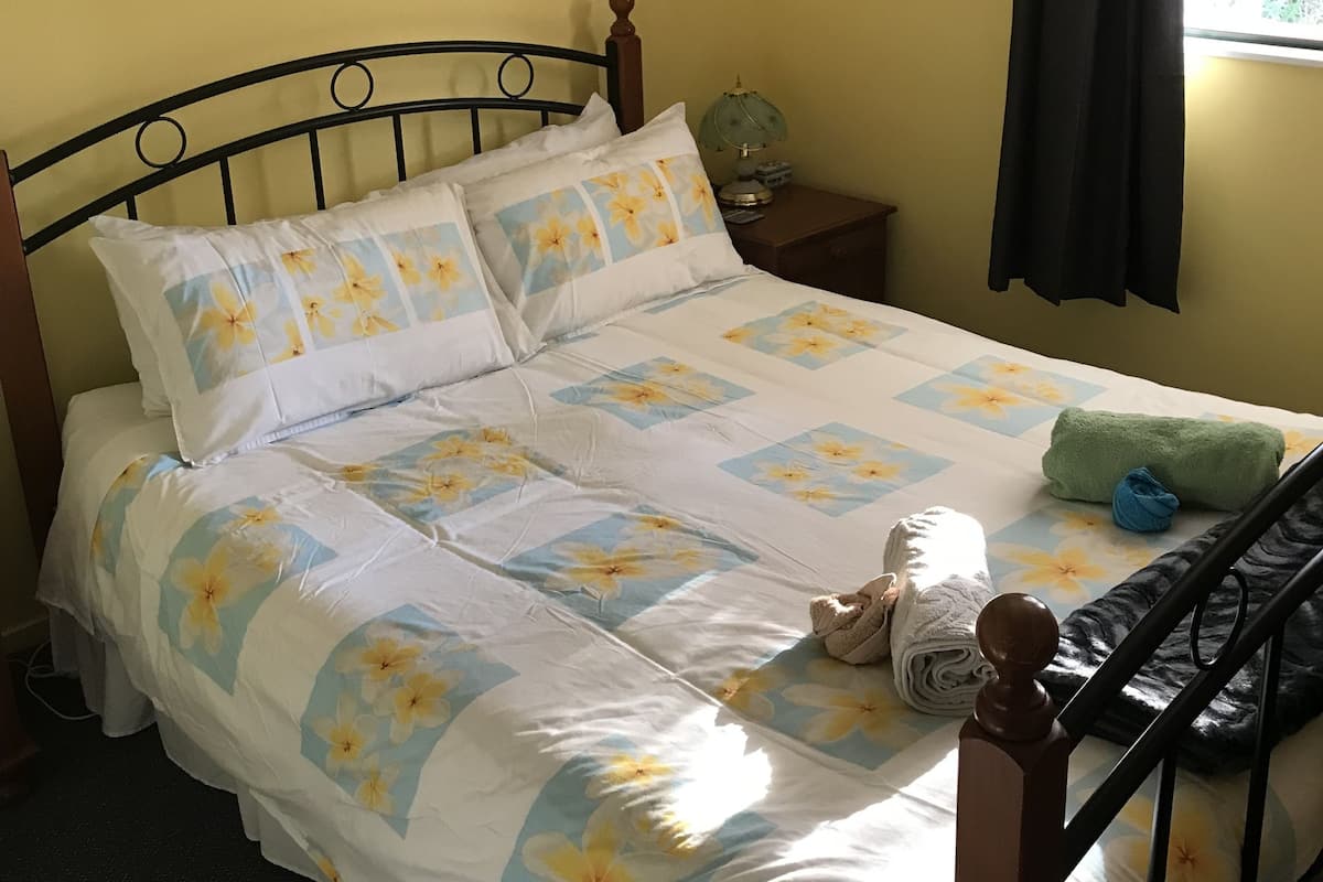 A bed with floral bedding, a nightstand with a lamp, a poster on the wall, and a window with curtains.