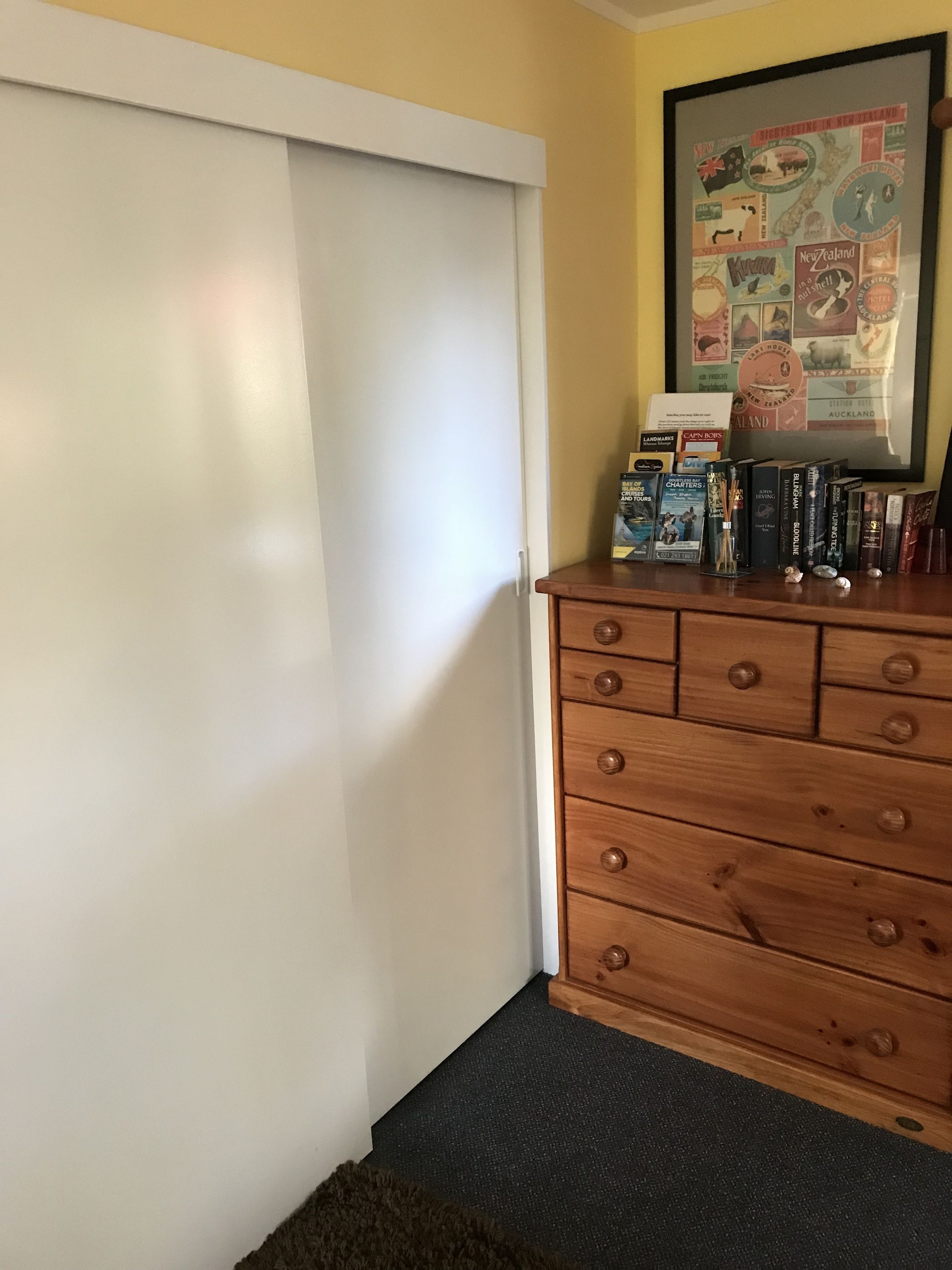 A room with a wooden dresser, a framed map on the wall, and a door.