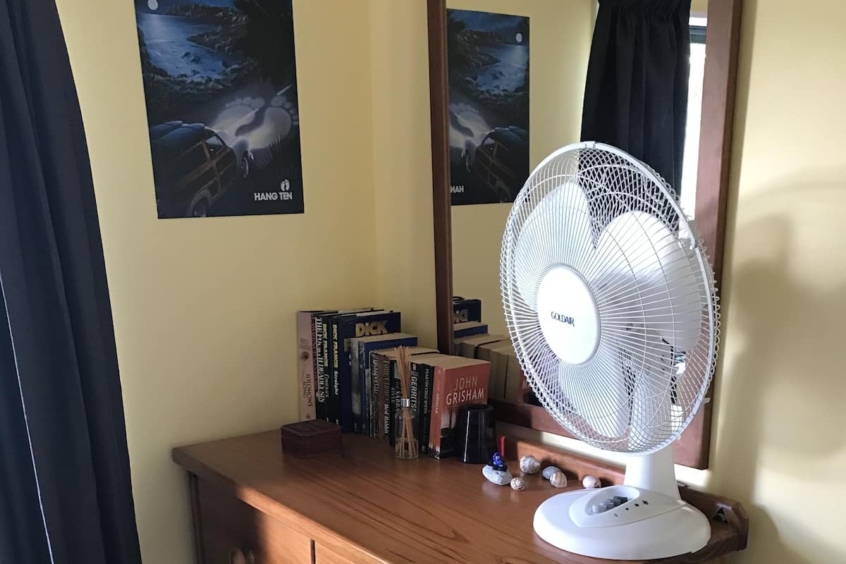 A wooden dresser with a white fan, books, and a mirror.