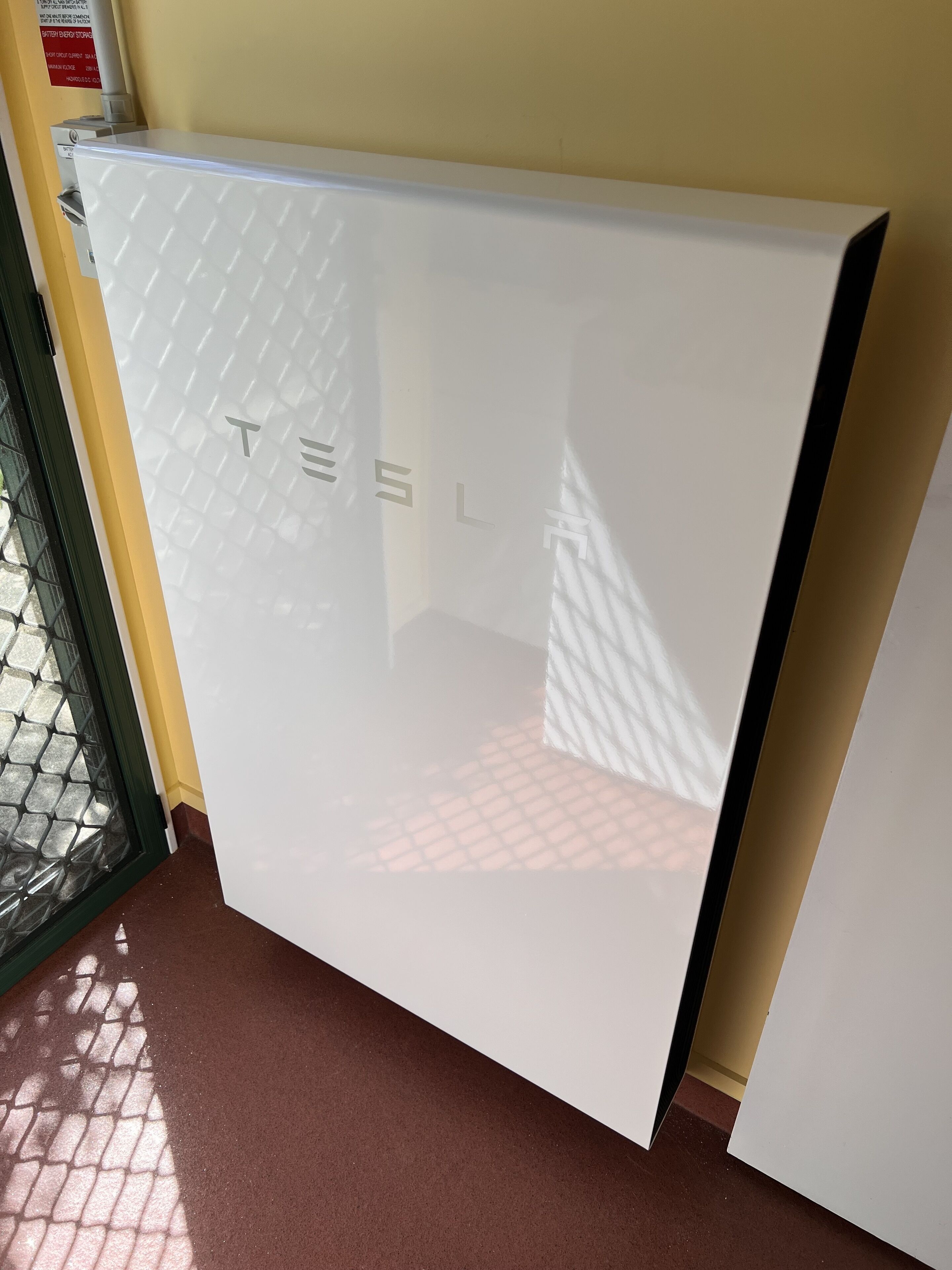 Une borne de recharge pour véhicules électriques Tesla, de couleur blanche, avec une finition métallique et le logo Tesla.