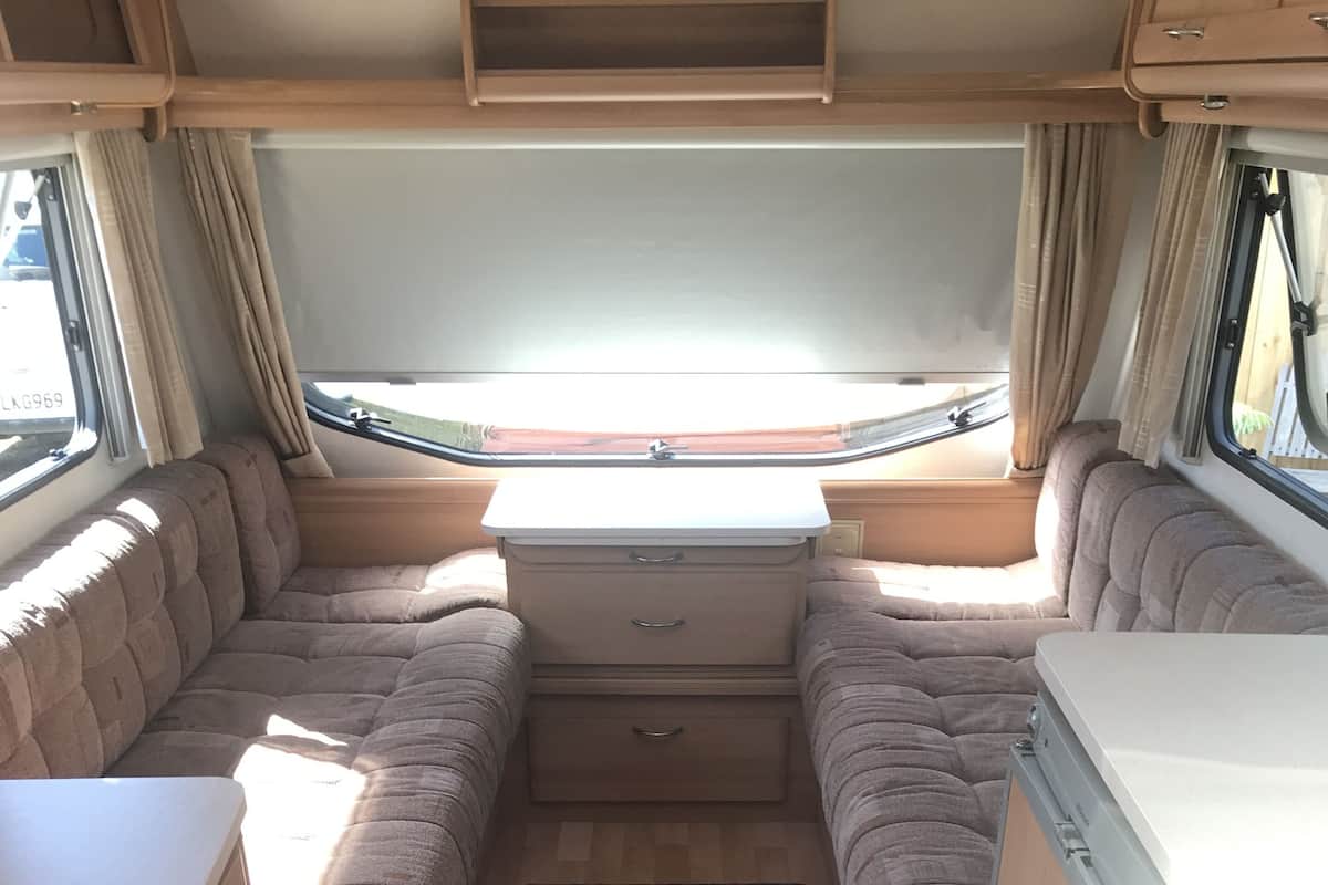 A compact RV interior with a kitchenette, seating area, and a window.