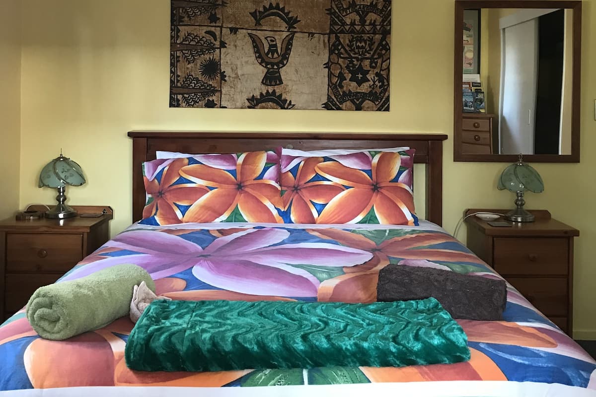 A bed with a colorful floral bedspread, a tapestry on the wall, and two bedside tables with lamps.