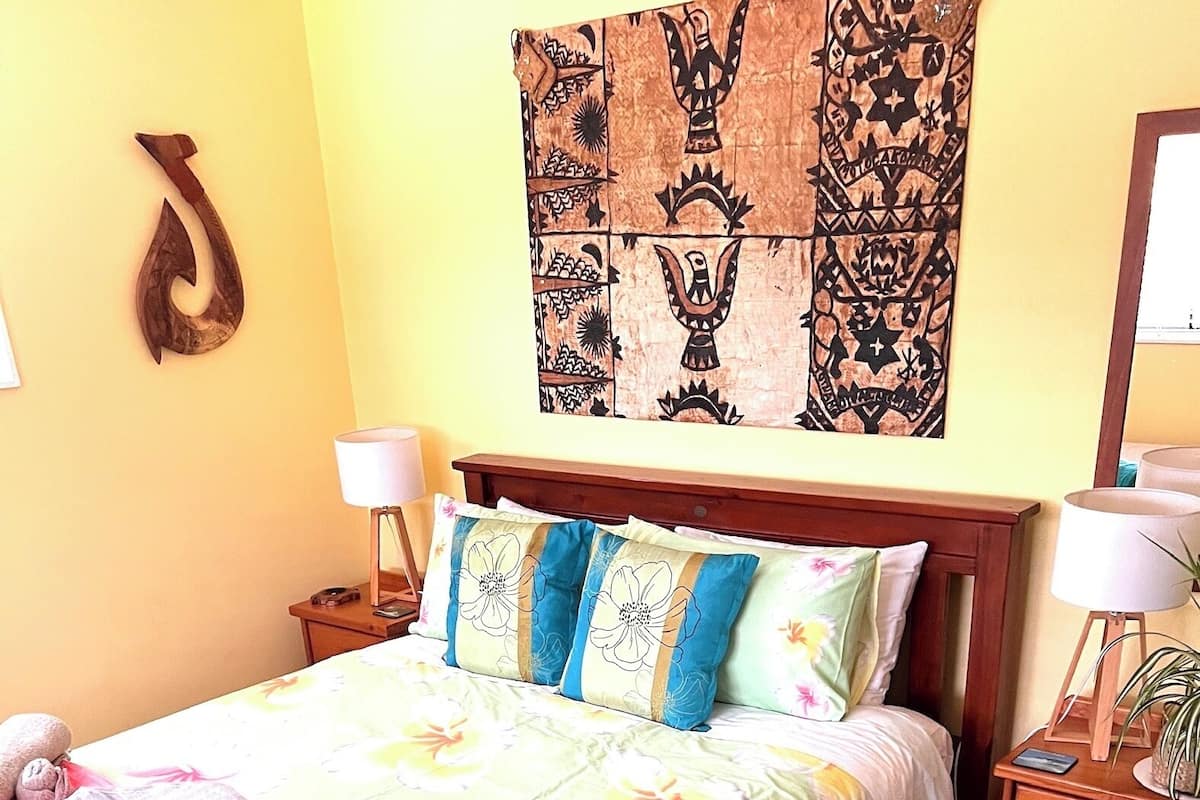 A neatly made bed with floral bedding, two pillows, a bedside lamp, and a wooden nightstand with a lamp.