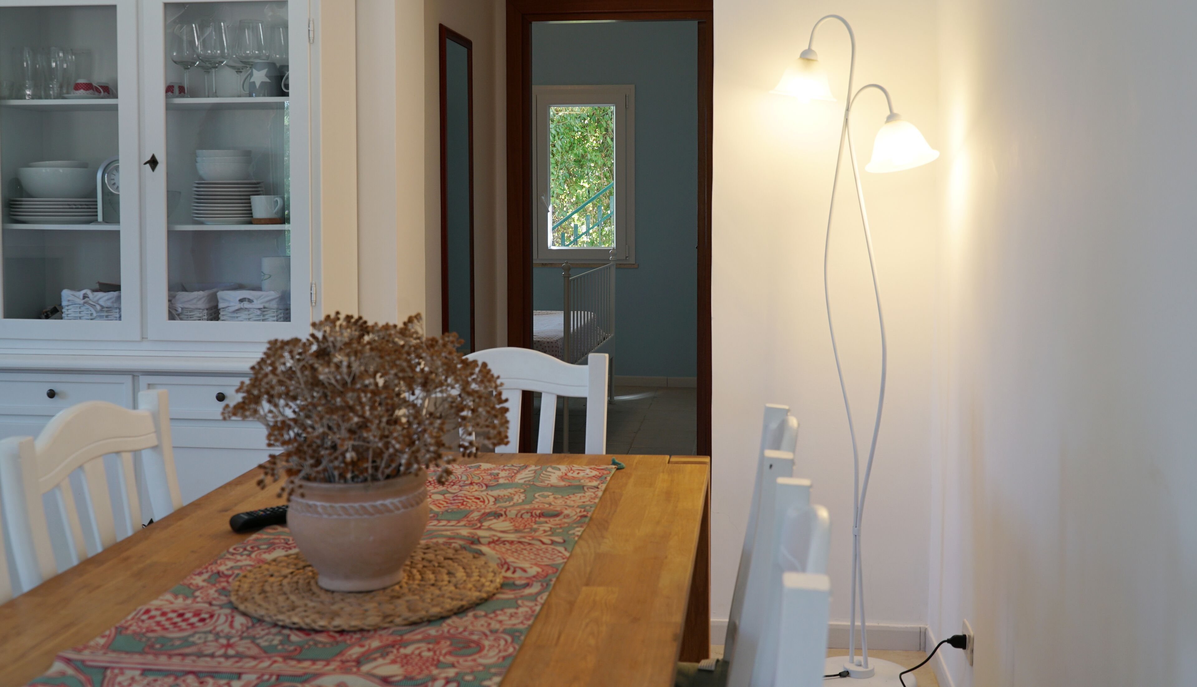 A dining area with a wooden table, chairs, a potted plant, and a lamp.