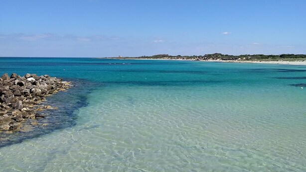 Ein freier Blick auf einen Strand mit felsigem Ufer und ruhigem türkisblauem Wasser.
