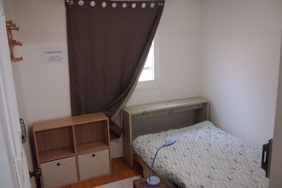 A small, compact bedroom with a single bed, a desk, and a storage unit.