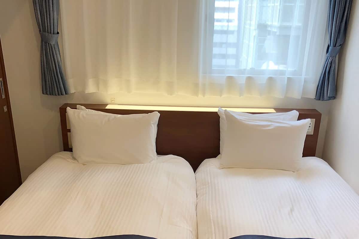 Una cama doble con dos almohadas, cabecera de madera y ventana con cortinas.