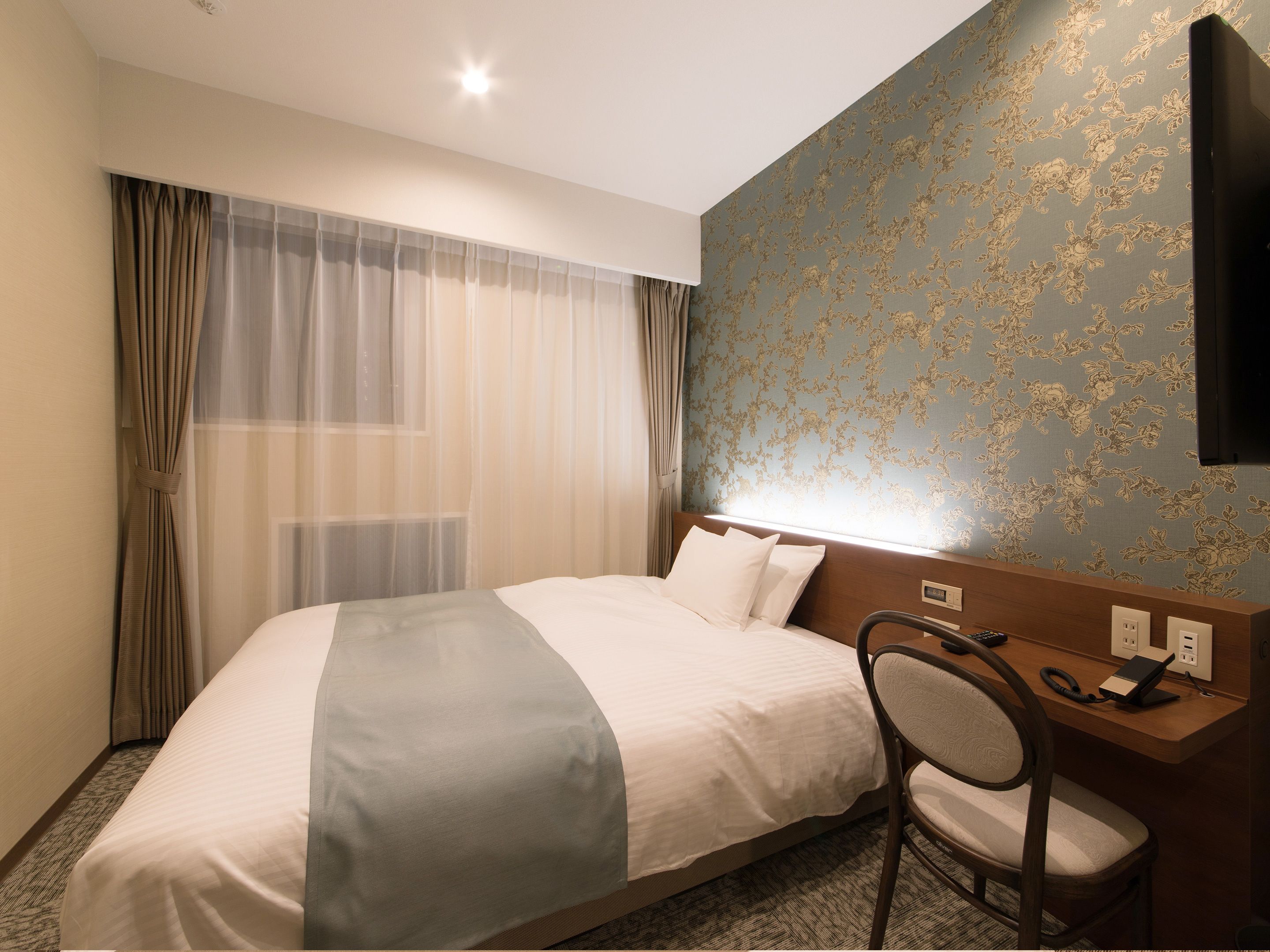 A hotel room with a bed, a desk, and a chair.
