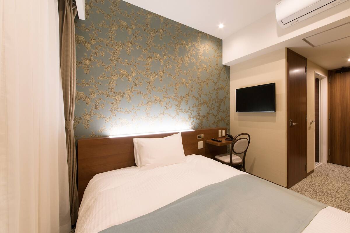 Habitación de hotel con cama, escritorio, silla, televisión y aire acondicionado.