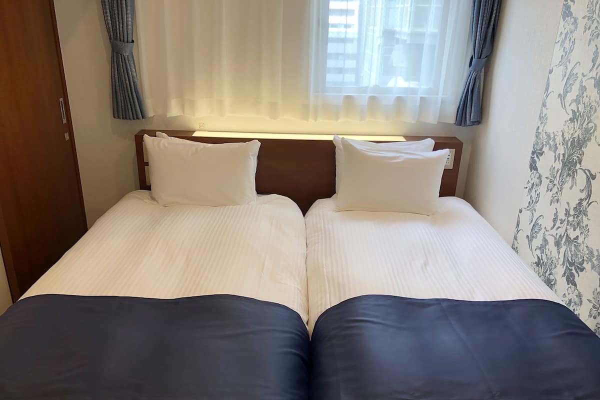 Cama doble con ropa de cama blanca y cabeceros oscuros en una habitación de hotel.