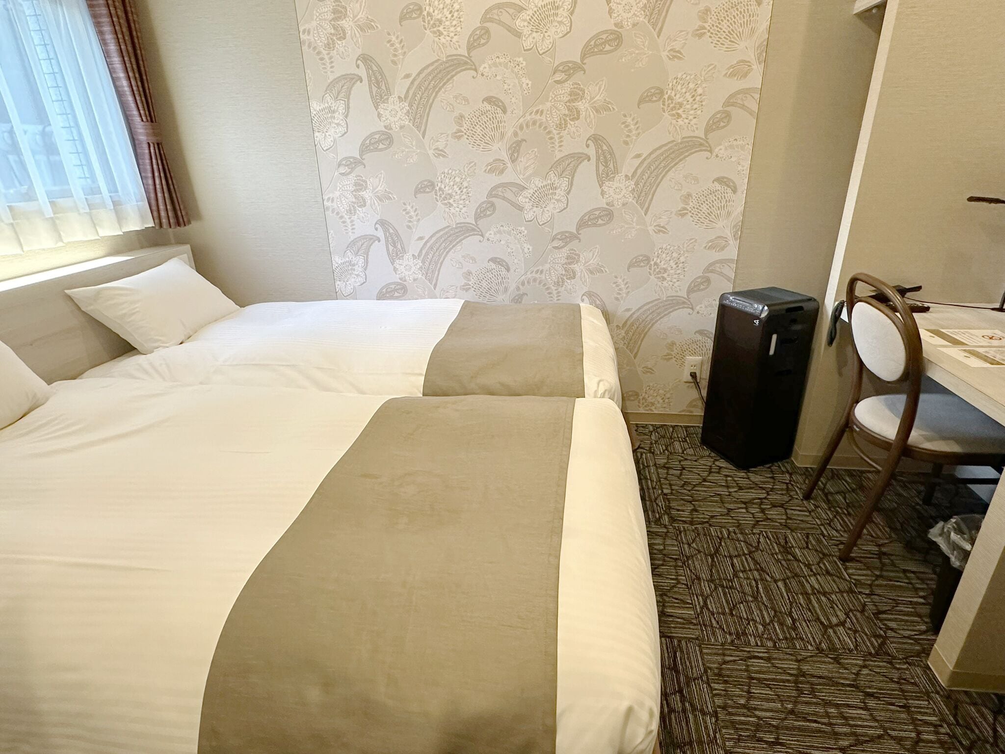 A hotel room with two beds, a desk, a chair, and a large speaker.