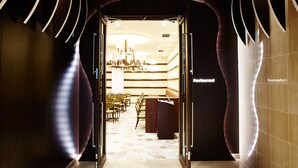 A modern restaurant with a sleek interior, featuring a long dining area with chairs and tables, a central chandelier, and a sign indicating the restaurant name. - S Training Center Hotel Osaka (Osaka)