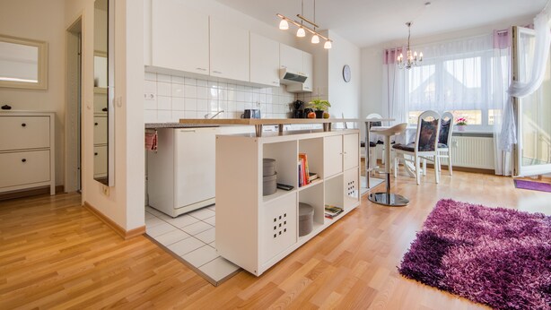 A modern kitchen with white cabinets, a wooden countertop, and a built-in island. There is a dining area with a table and chairs, and a purple rug on the floor.