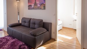 A modern living room with a grey sofa, a purple rug, and a cityscape painting on the wall.