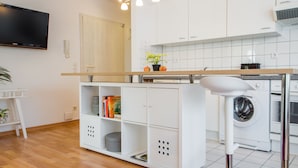A modern kitchen with white cabinets, a built-in washing machine, and a flat-screen TV mounted on the wall.