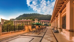 A terrace with outdoor seating, a view of a building with a red roof, and a mountain in the background. - Felton Grand Hotel Bazhong (Bazhong)