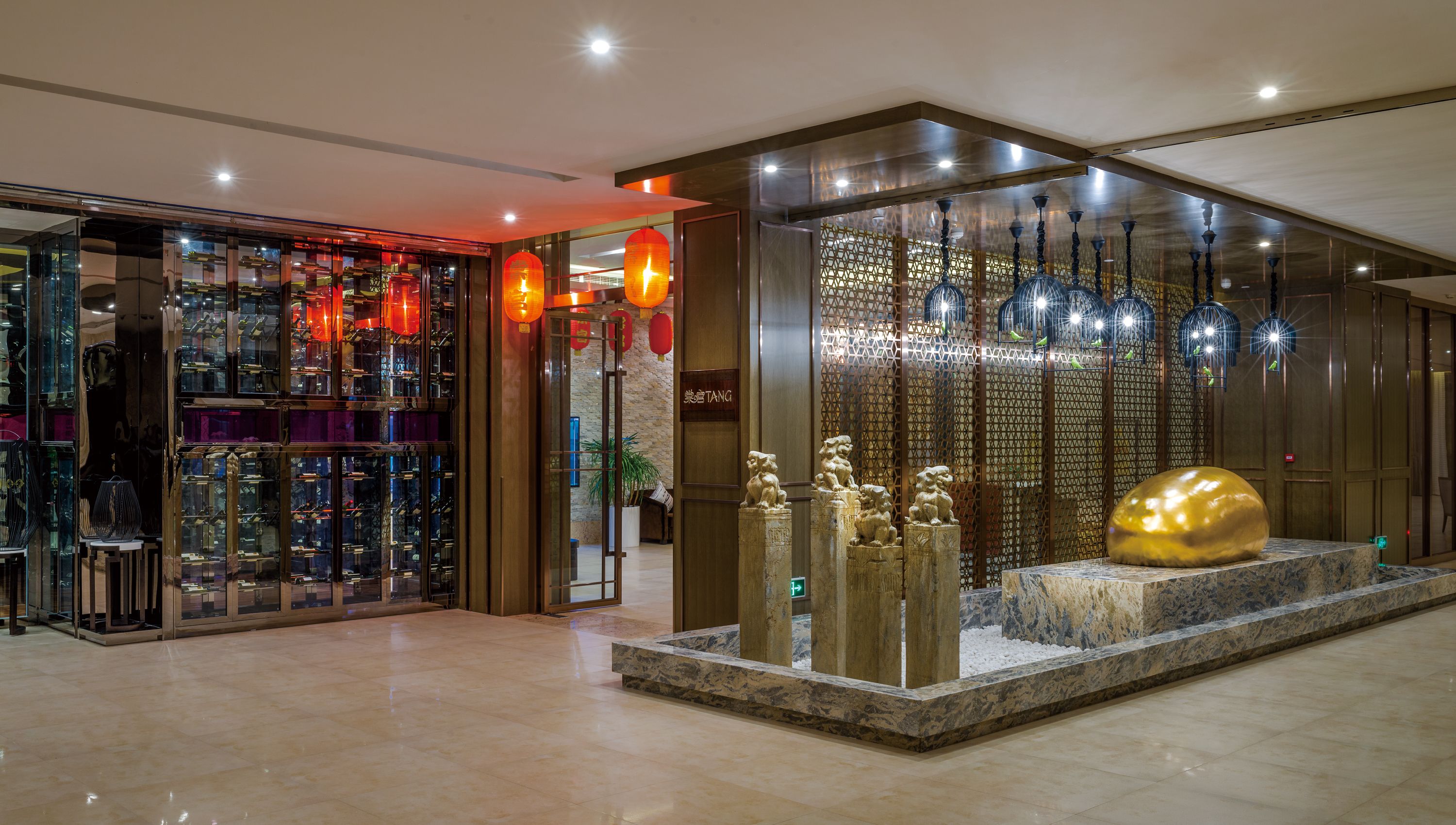 A modern hotel lobby with a glass storefront displaying various items, a decorative wall with hanging lights, and a stone sculpture centerpiece.