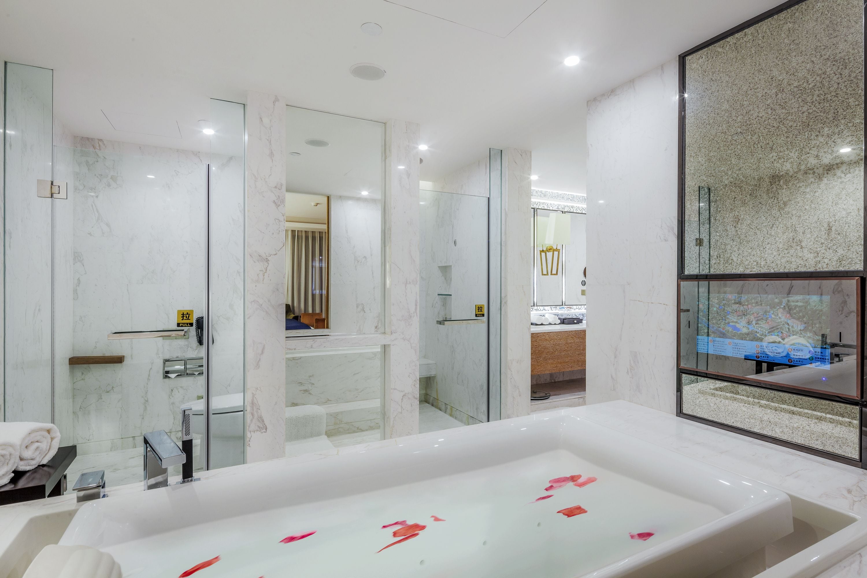 A modern bathroom with a large bathtub, glass shower enclosure, and a mirror with a cityscape view.