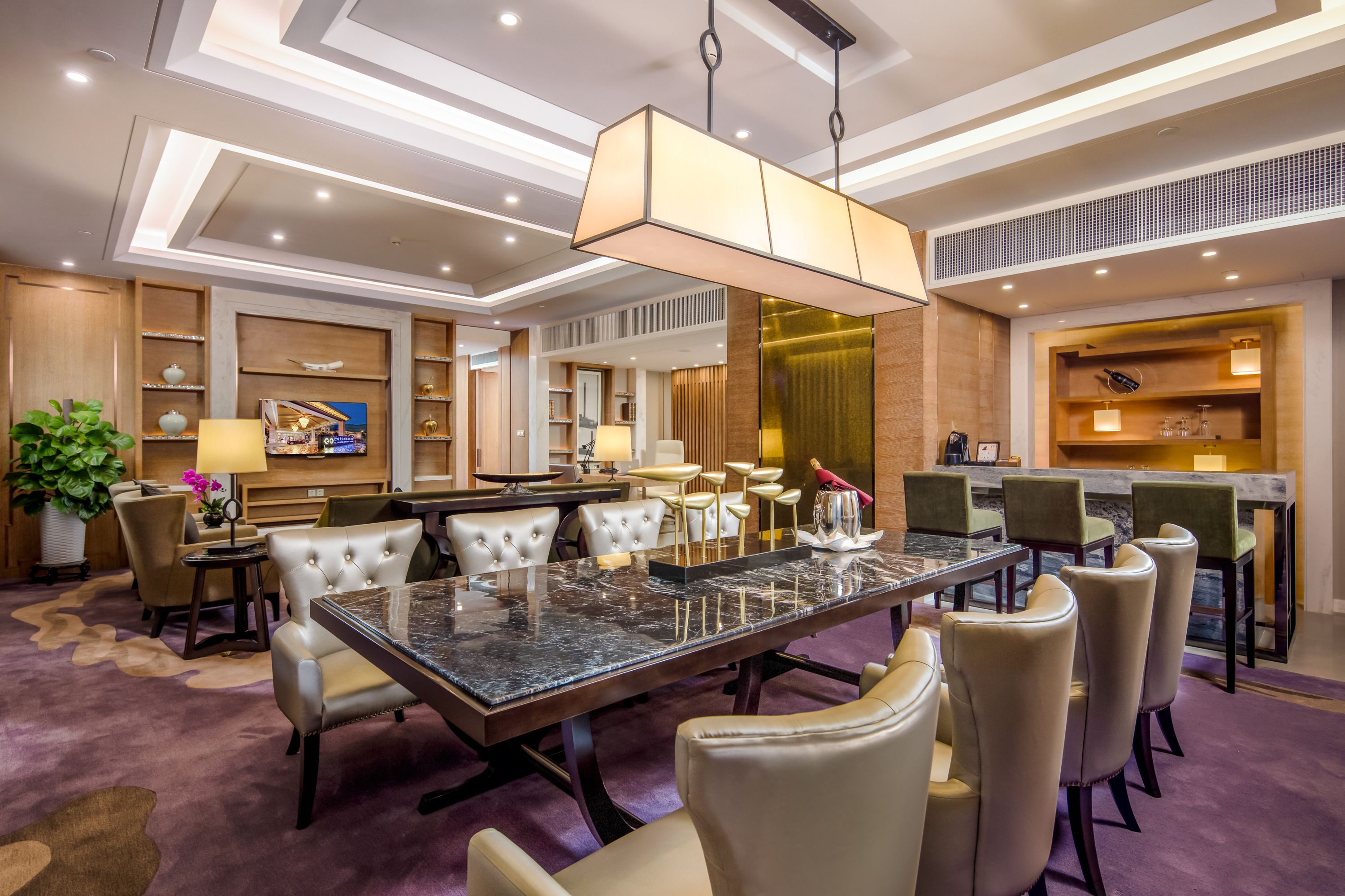 A modern hotel lobby with a marble reception desk, leather seating, and a large chandelier.