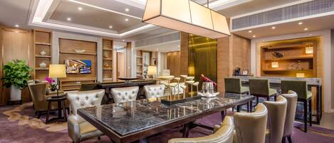 A modern hotel lobby with a marble reception desk, leather seating, and a large chandelier.