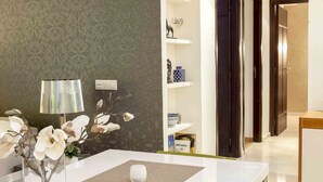 Een moderne eetruimte met een witte tafel, een glazen vaas met bloemen en een behang met patroon.
