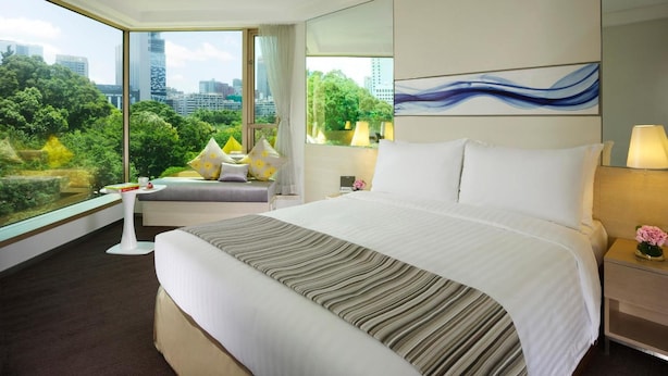 Een hotelkamer met een groot bed, stadszicht en een raam met uitzicht op groen.