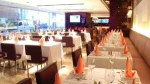 Een restaurant met meerdere tafels klaar voor diners, elk met witte tafellakens en oranje servetten.