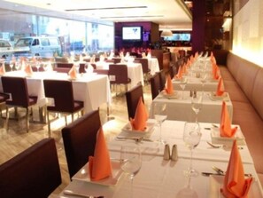 Een restaurant met meerdere tafels klaar voor diners, elk met witte tafellakens en oranje servetten.