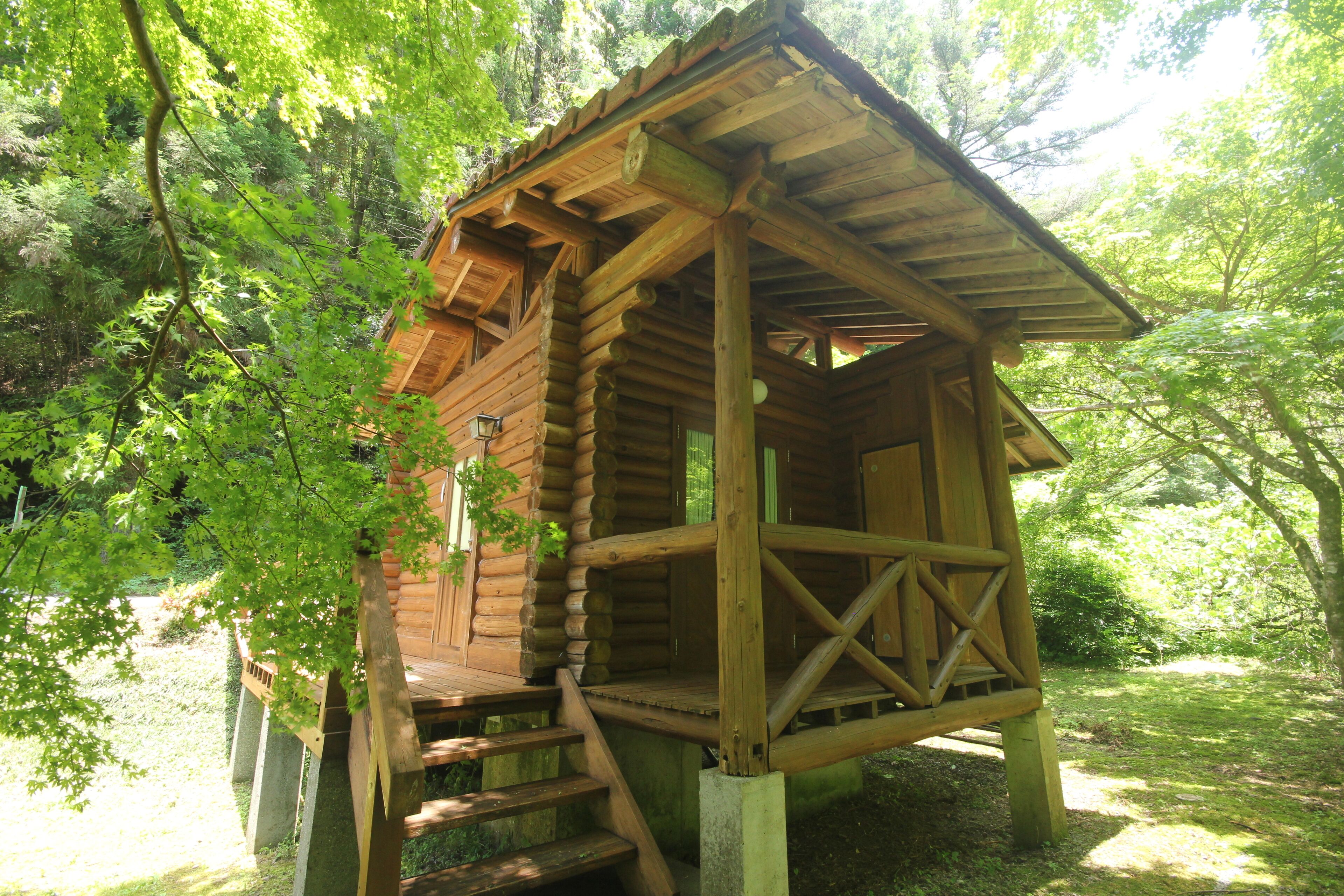 A wooden cabin with a sloped roof, built into a forested area.