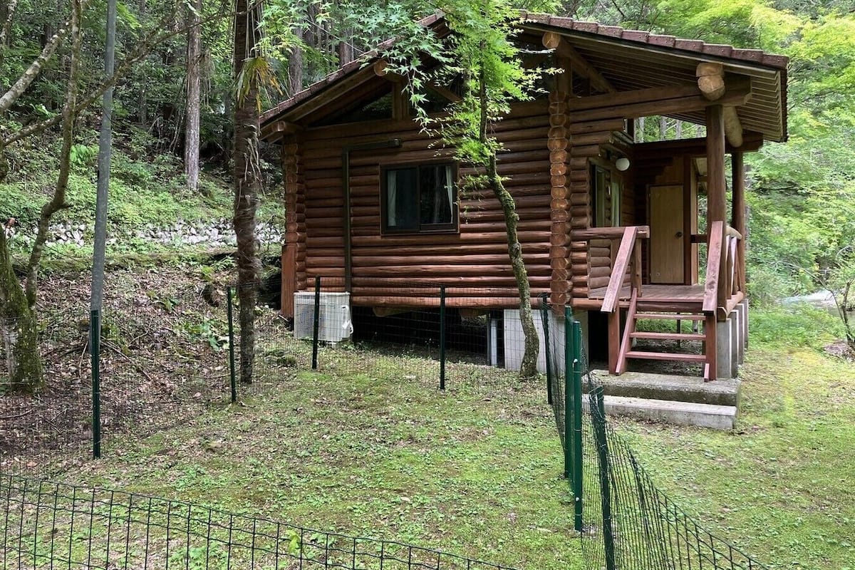 Una cabaña rústica de troncos con un porche, rodeada de un bosque.