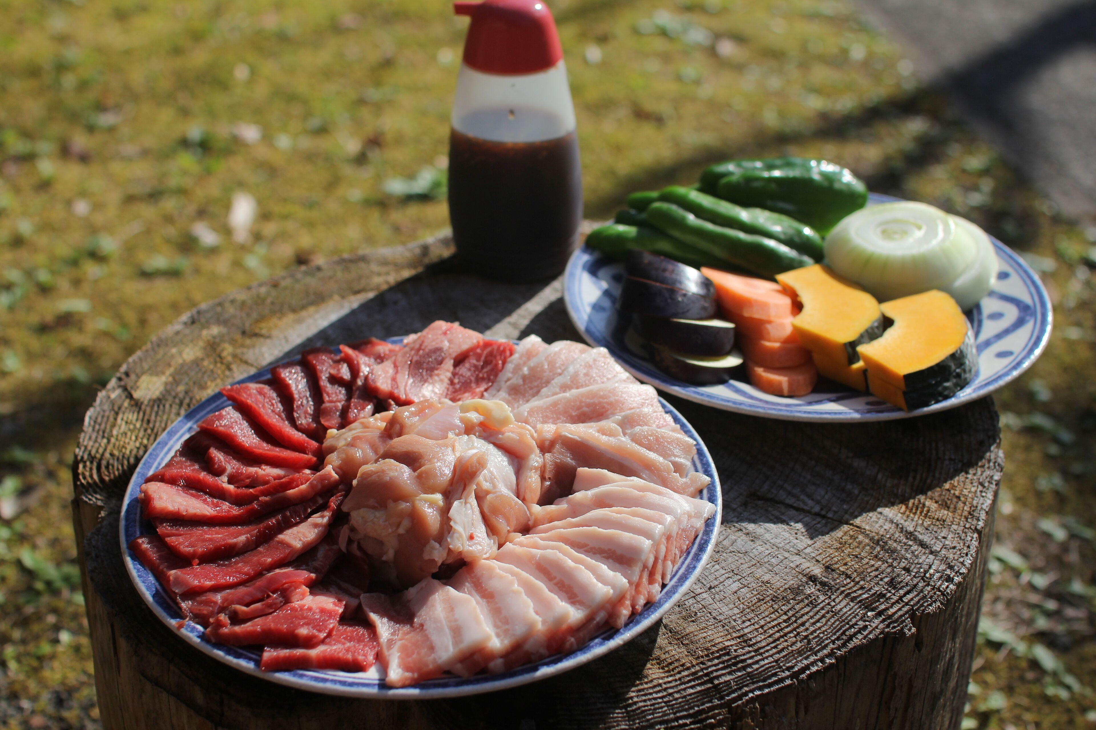 Une assiette de viande tranchée, de légumes et une bouteille de sauce, le tout posé sur un tronc d’arbre.
