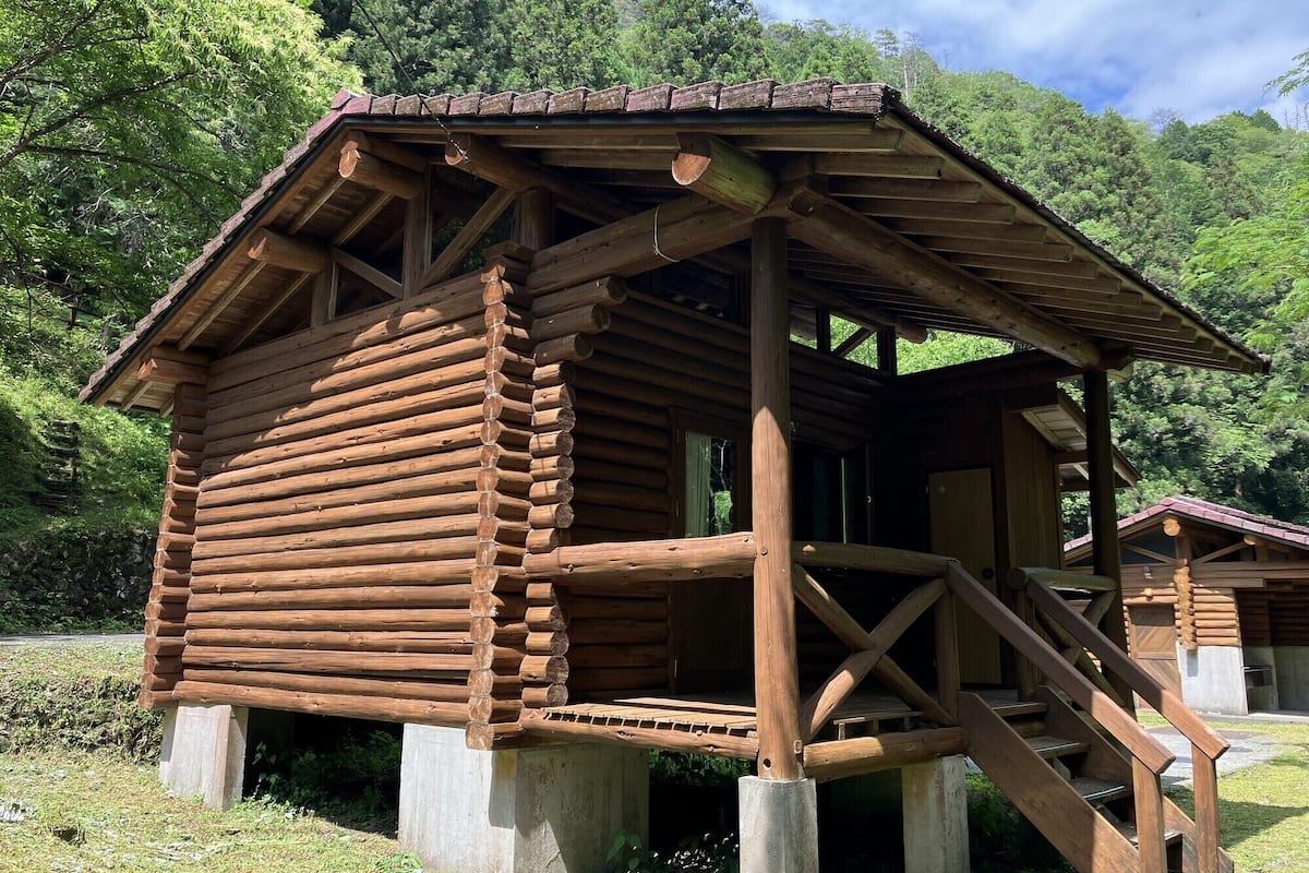Una cabaña de madera con porche y escaleras, rodeada de vegetación.