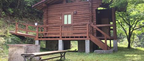 A wooden cabin with a balcony, a bench, and a small table.