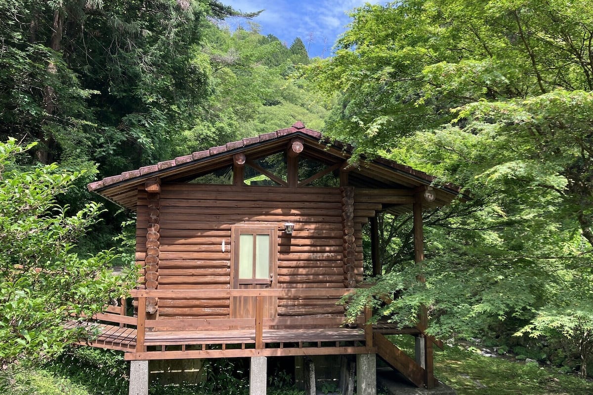 Una cabaña de madera con un porche, rodeada de un bosque denso.