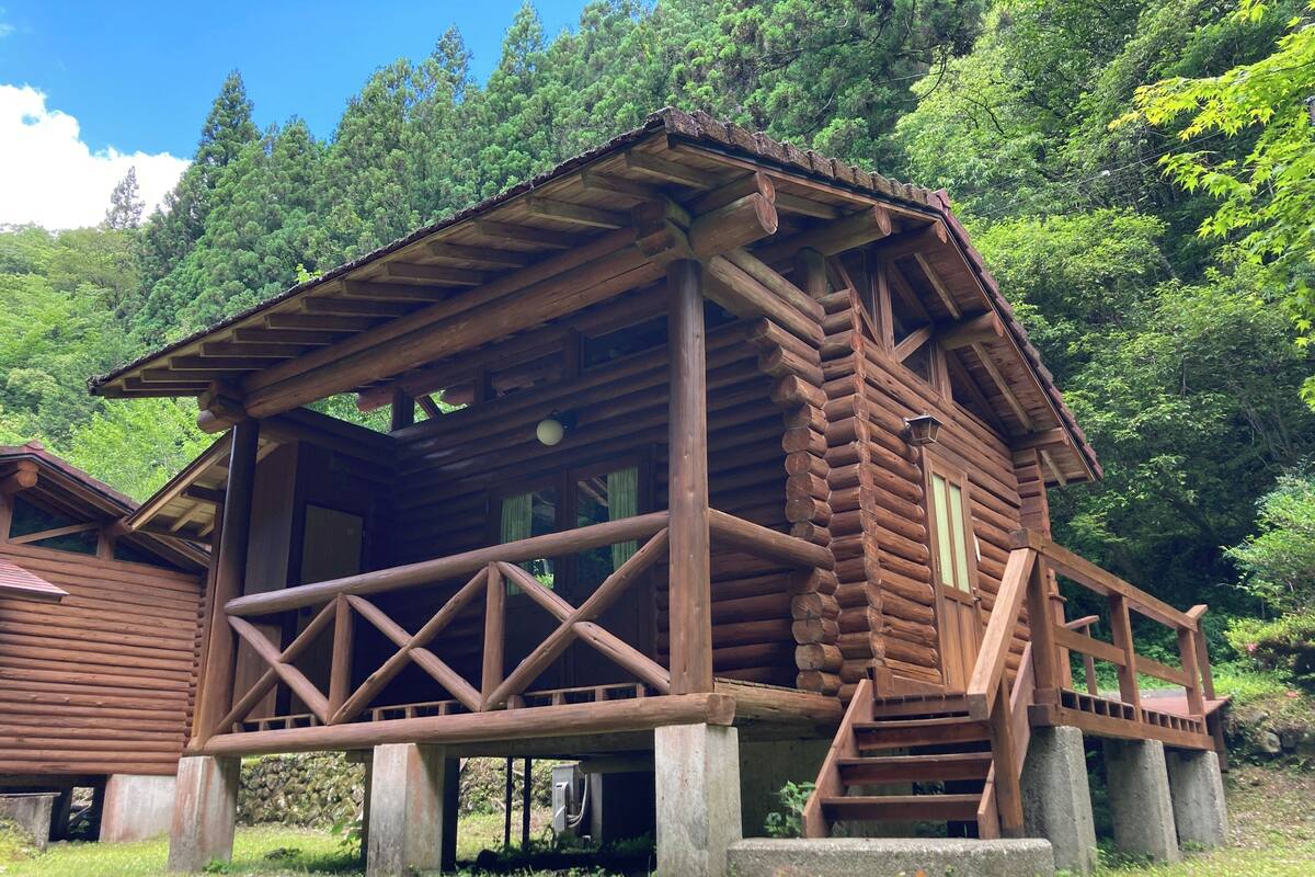 Una cabaña de madera con balcón, rodeada de exuberante vegetación.
