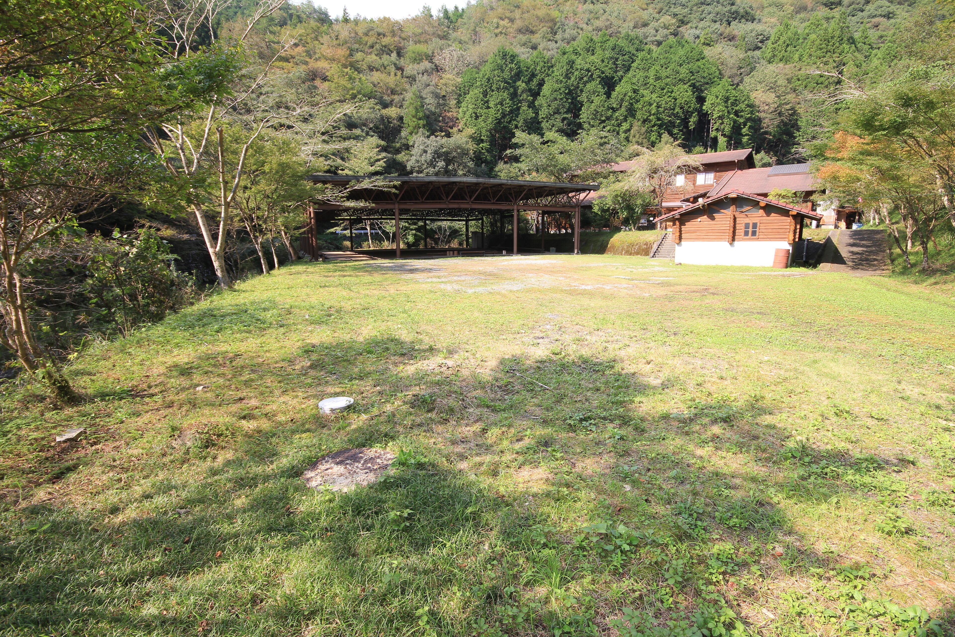 A rustic wooden cabin with a covered porch, surrounded by a grassy area and dense forest.